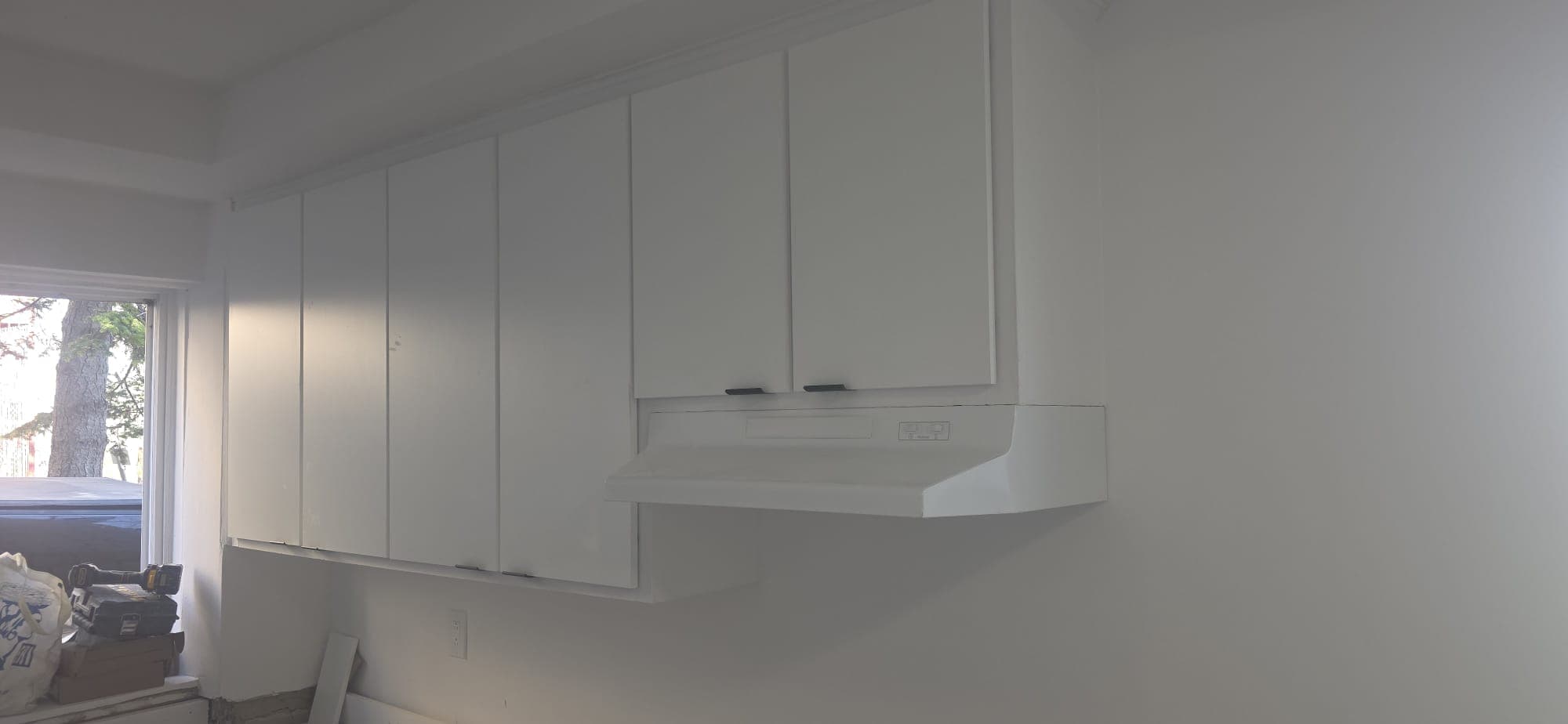 Upper cabinets and range hood installed on a freshly finished kitchen wall.